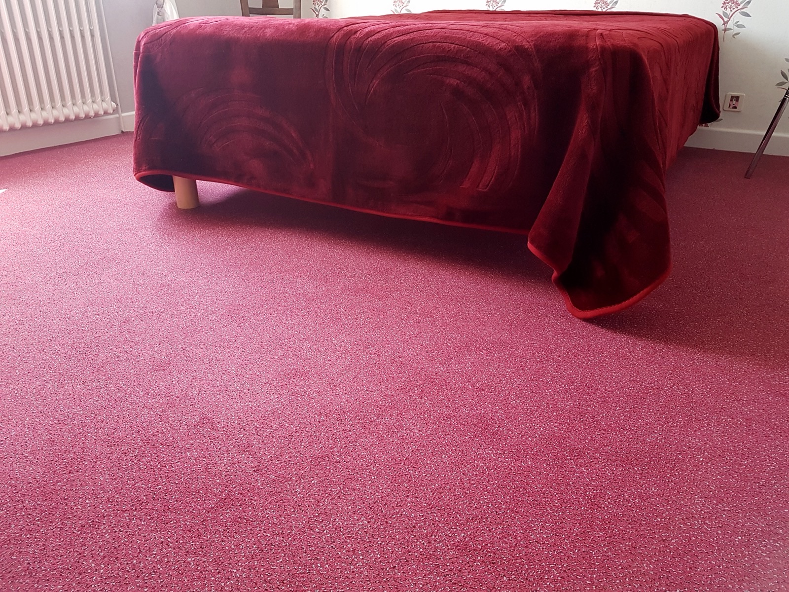 Chambre avec une moquette rose framboise au pied d'un lit couvert d'un plaid bordeaux