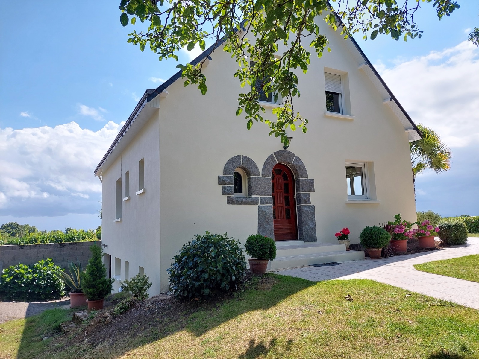Façade enduite claire avec porte d'entrée en bois encadrée de granit et petite fenêtre cintrée