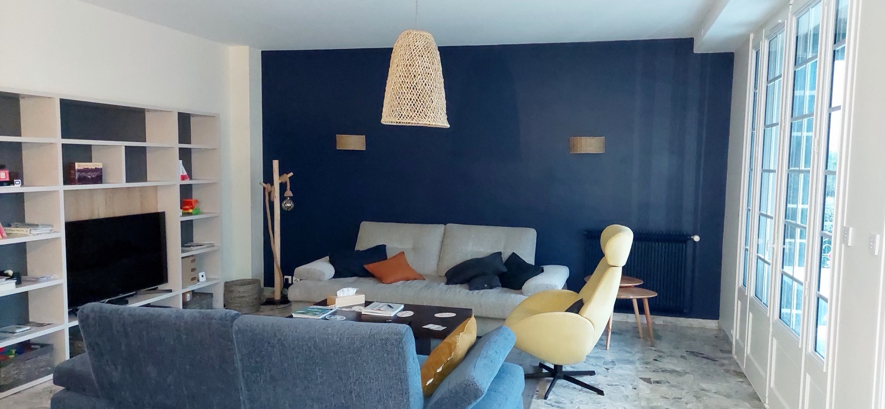 Salon avec un mur d'accent bleu nuit, bibliothèque blanche et fauteuil jaune