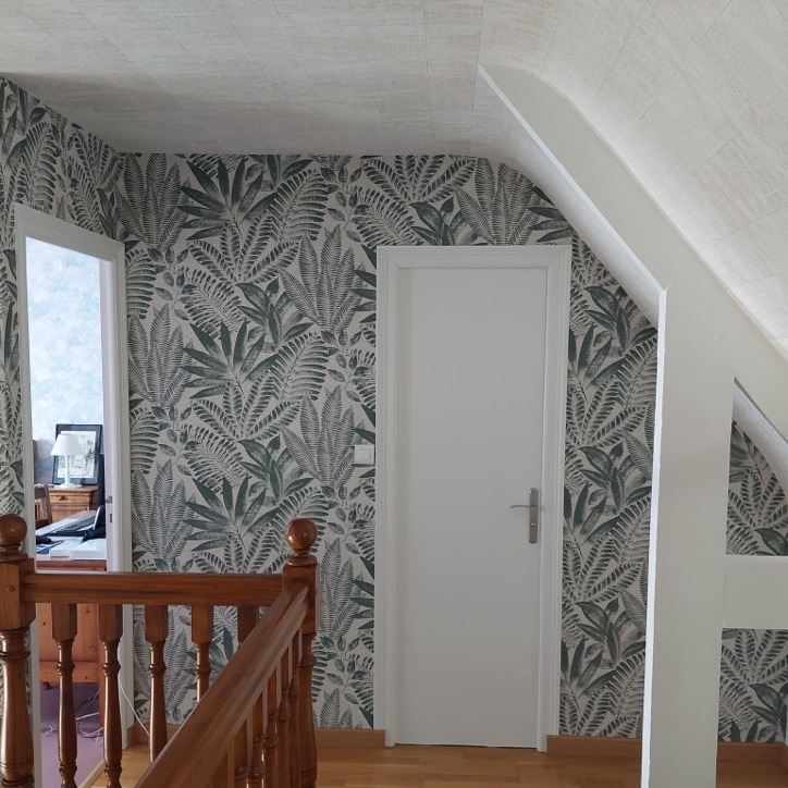 Palier sous combles avec papier peint à grandes feuilles vertes et rampe en bois