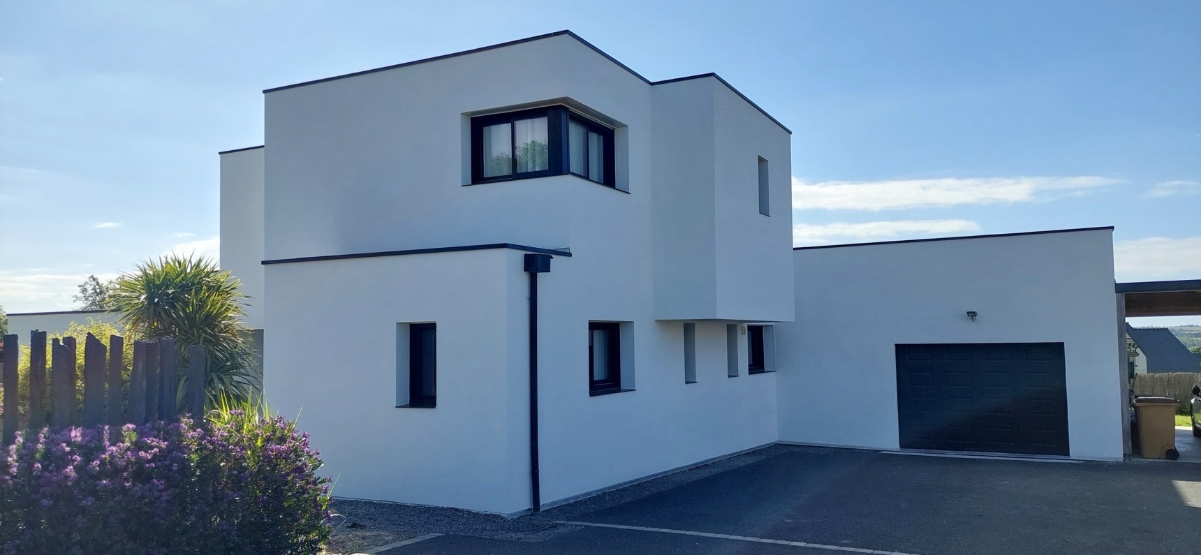 Maison contemporaine cubique à façade blanche et porte de garage anthracite sous un ciel bleu