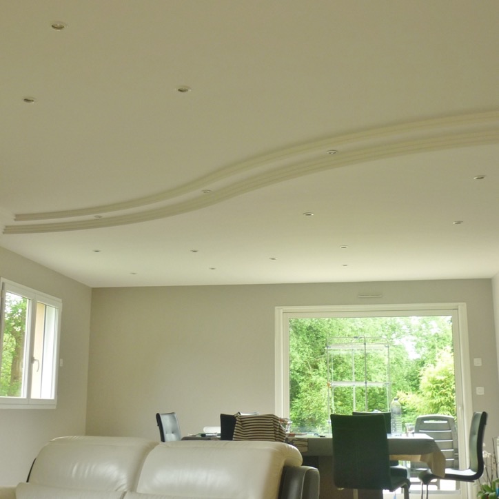 Plafond en staff dessinant une vague au-dessus d'un salon lumineux aux murs clairs