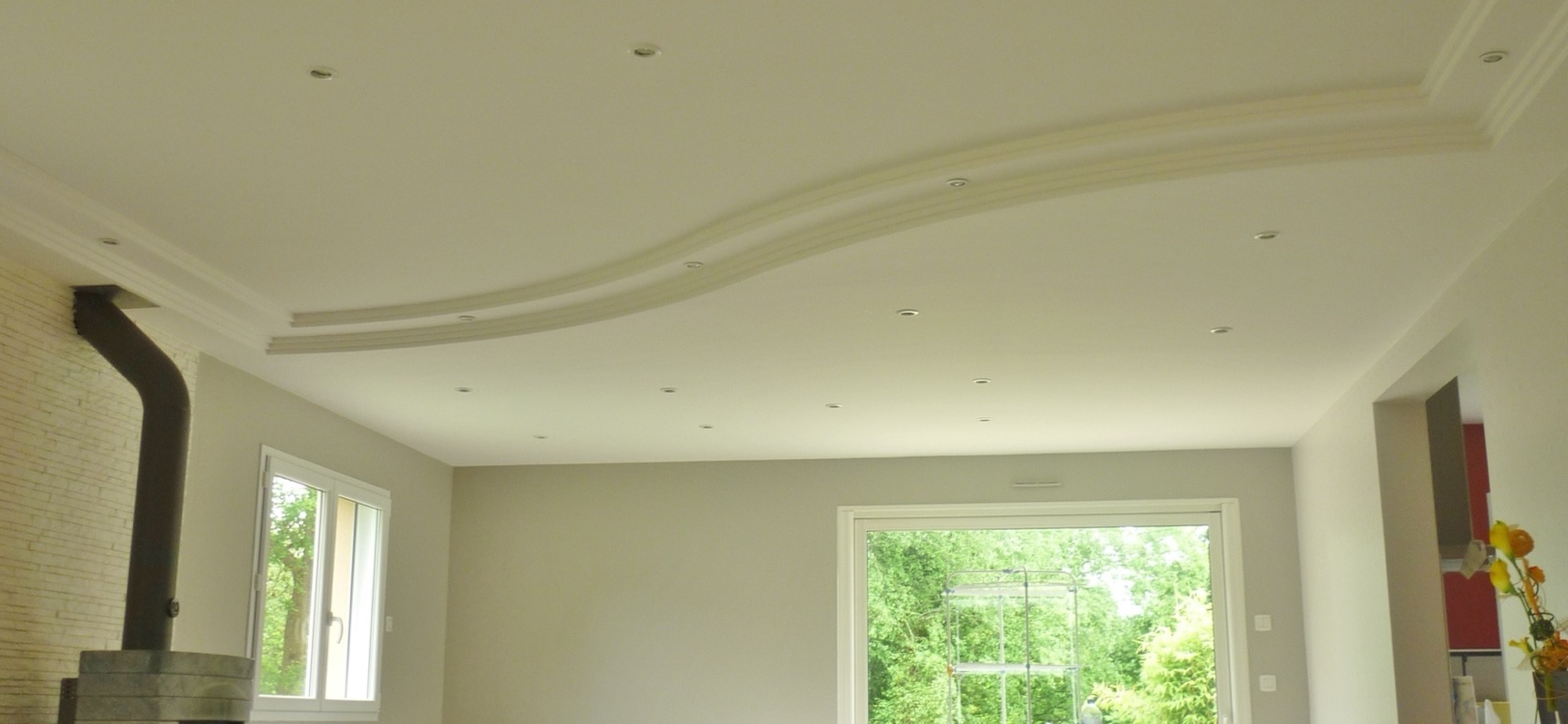 Plafond en staff dessinant une vague au-dessus d'un salon lumineux aux murs clairs