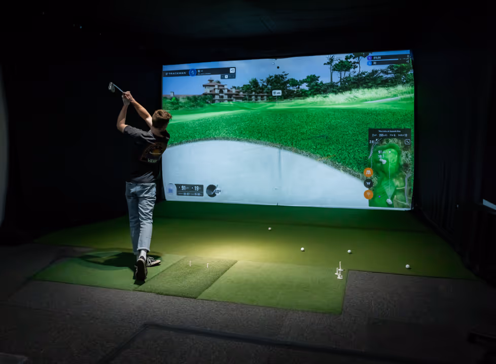 Two men playing golf at the GolfCave. One man is over the ball about to hit while the other watches