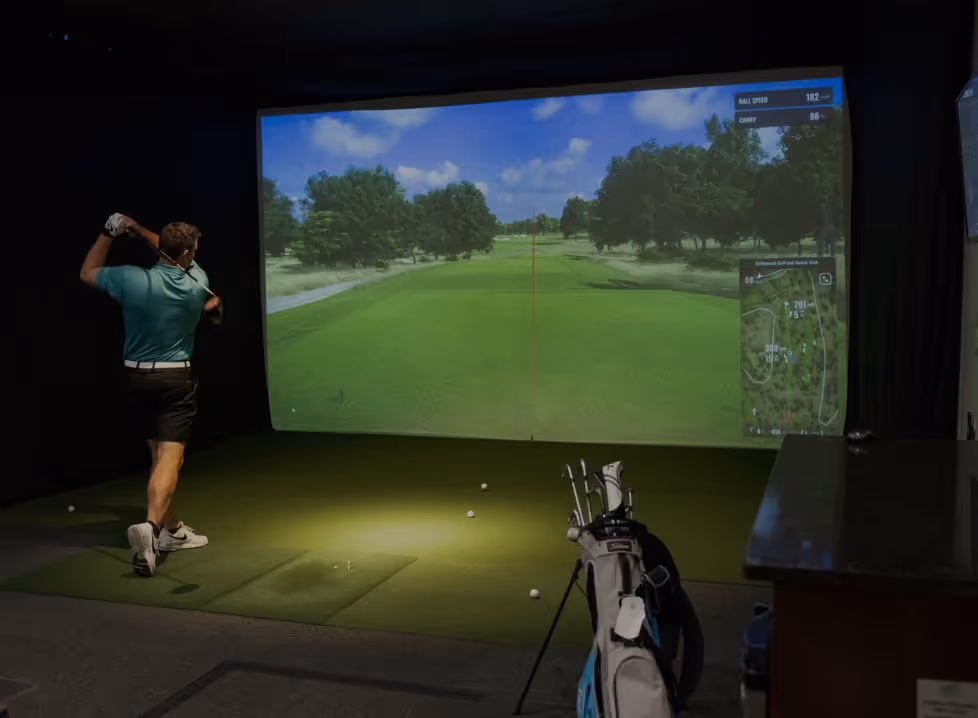 Two men playing golf at the GolfCave. One man is over the ball about to hit while the other watches