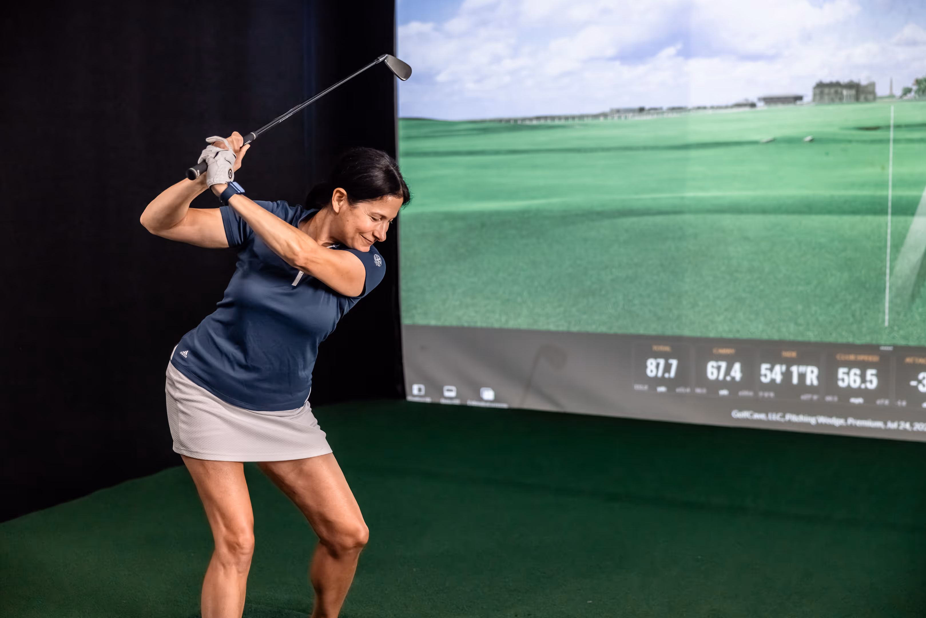 Two men playing golf at the GolfCave. One man is over the ball about to hit while the other watches