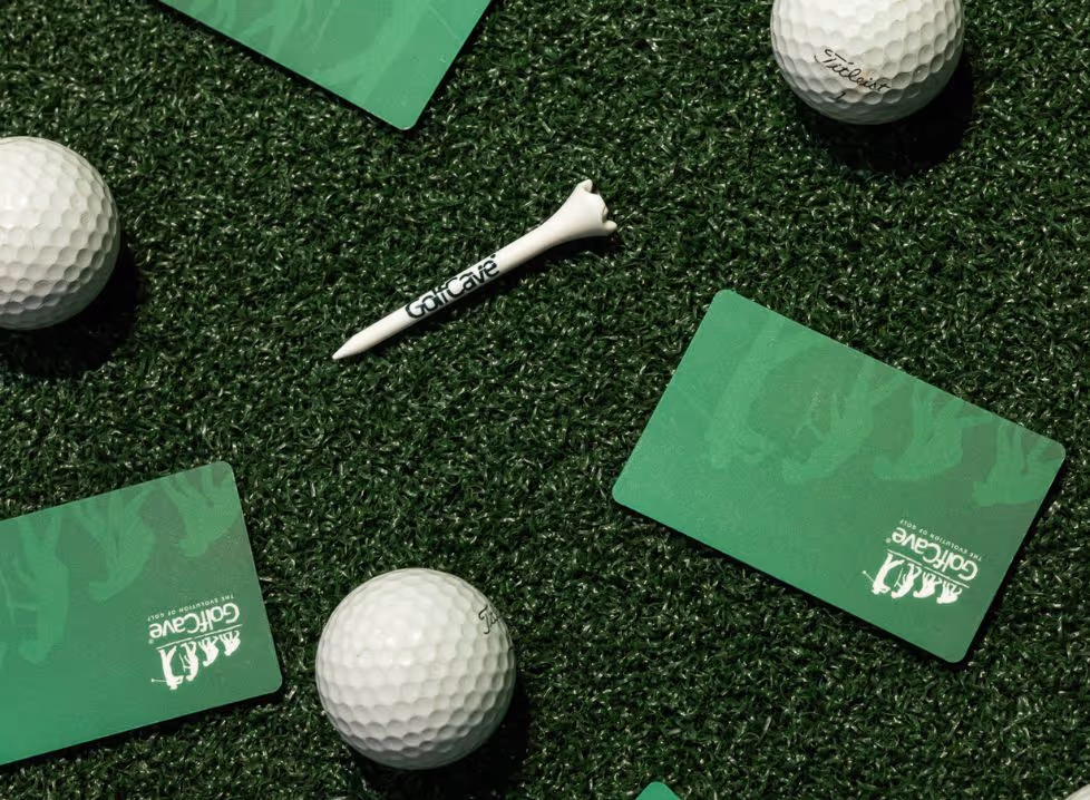 Two men playing golf at the GolfCave. One man is over the ball about to hit while the other watches