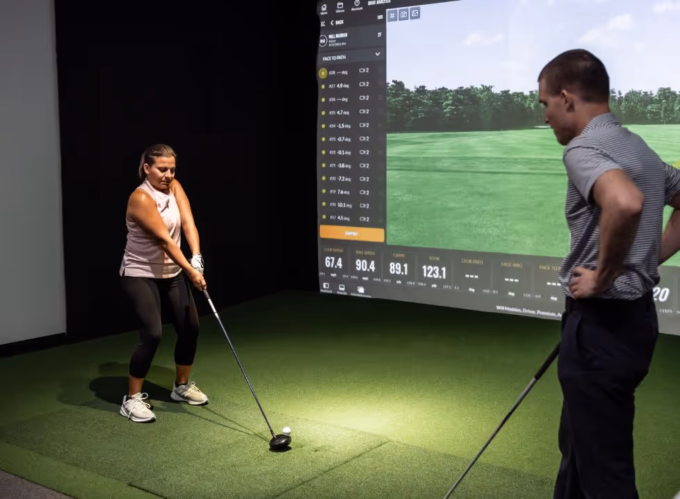 Two men playing golf at the GolfCave. One man is over the ball about to hit while the other watches