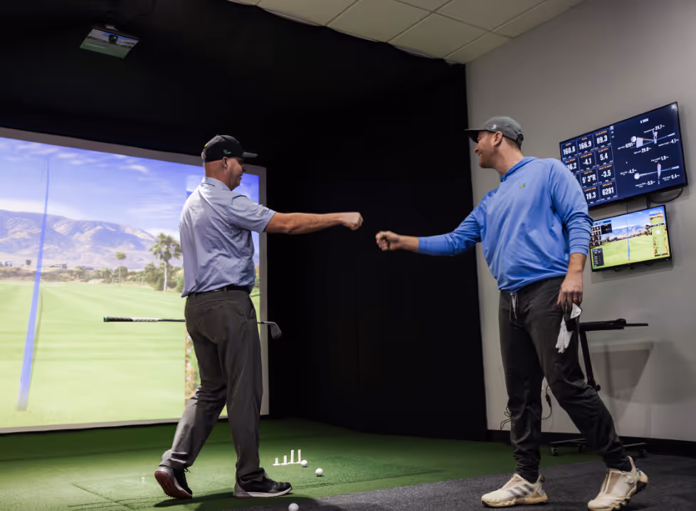 Two men playing golf at the GolfCave. One man is over the ball about to hit while the other watches