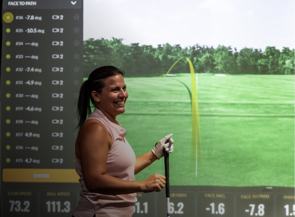 Two men playing golf at the GolfCave. One man is over the ball about to hit while the other watches