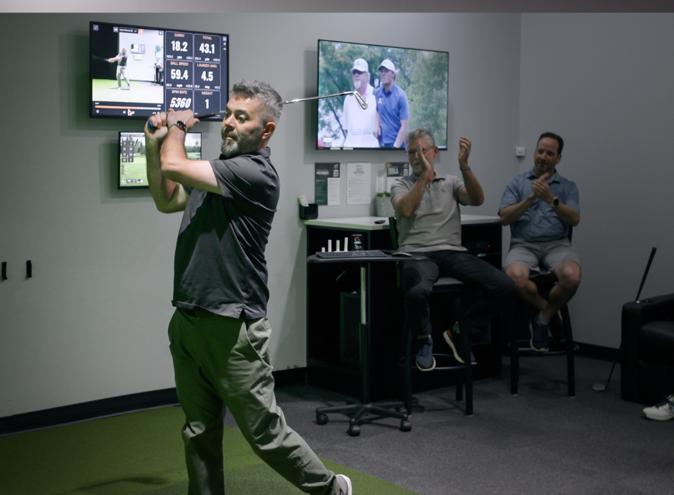Two men playing golf at the GolfCave. One man is over the ball about to hit while the other watches