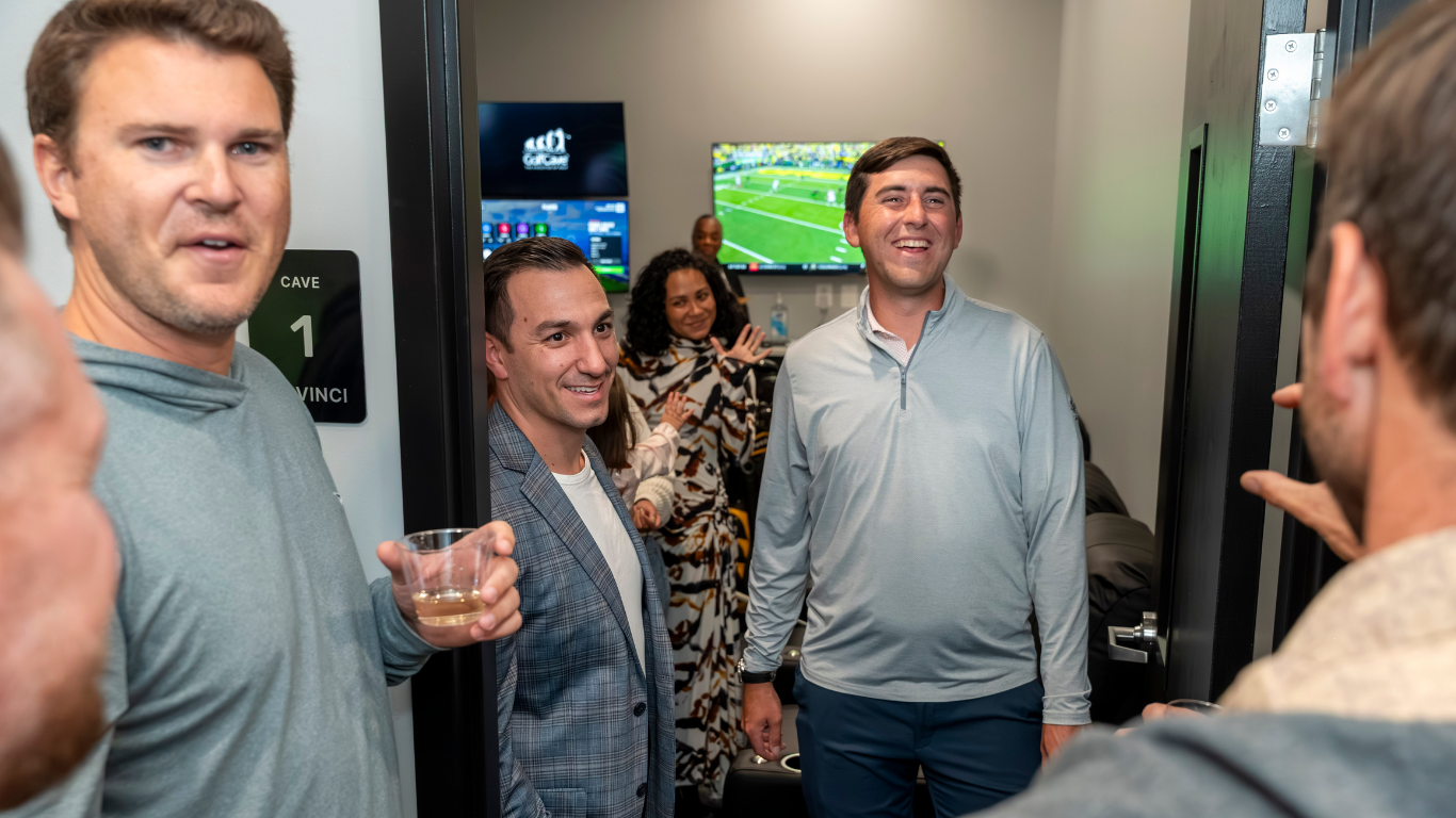 Two men playing golf at the GolfCave. One man is over the ball about to hit while the other watches