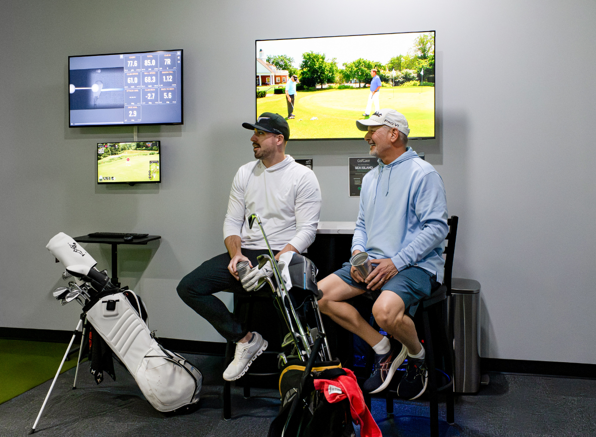 Two men playing golf at the GolfCave. One man is over the ball about to hit while the other watches