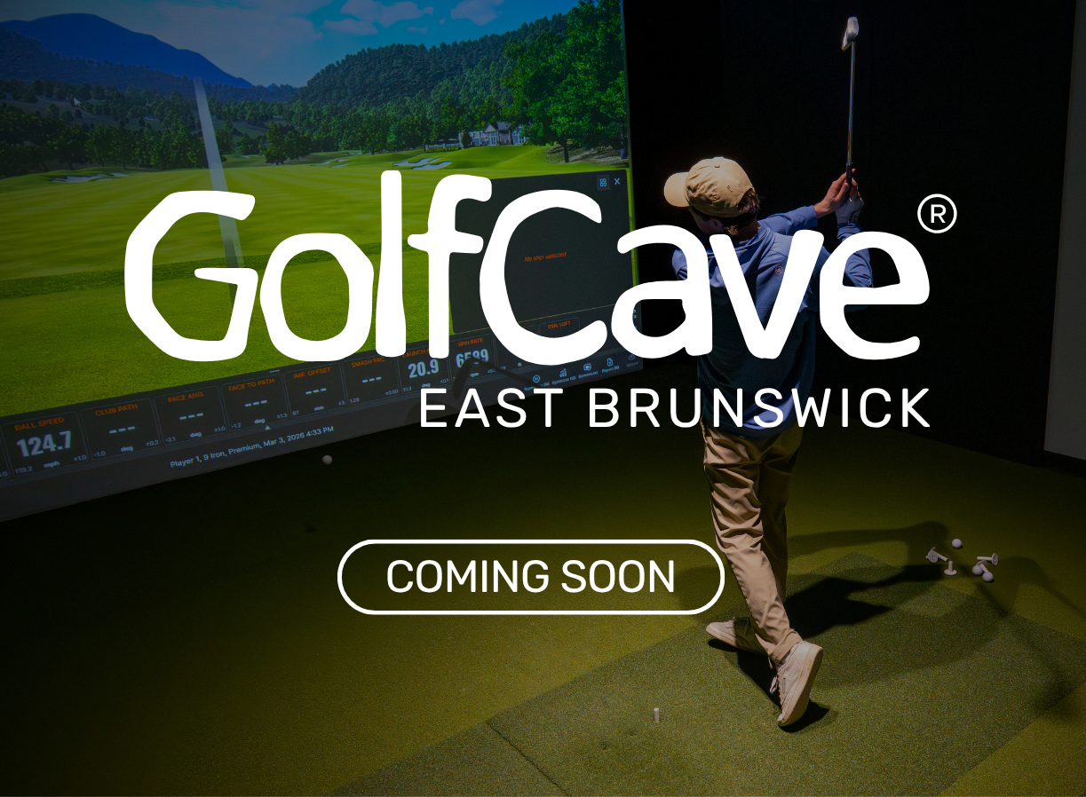 Two men playing golf at the GolfCave. One man is over the ball about to hit while the other watches