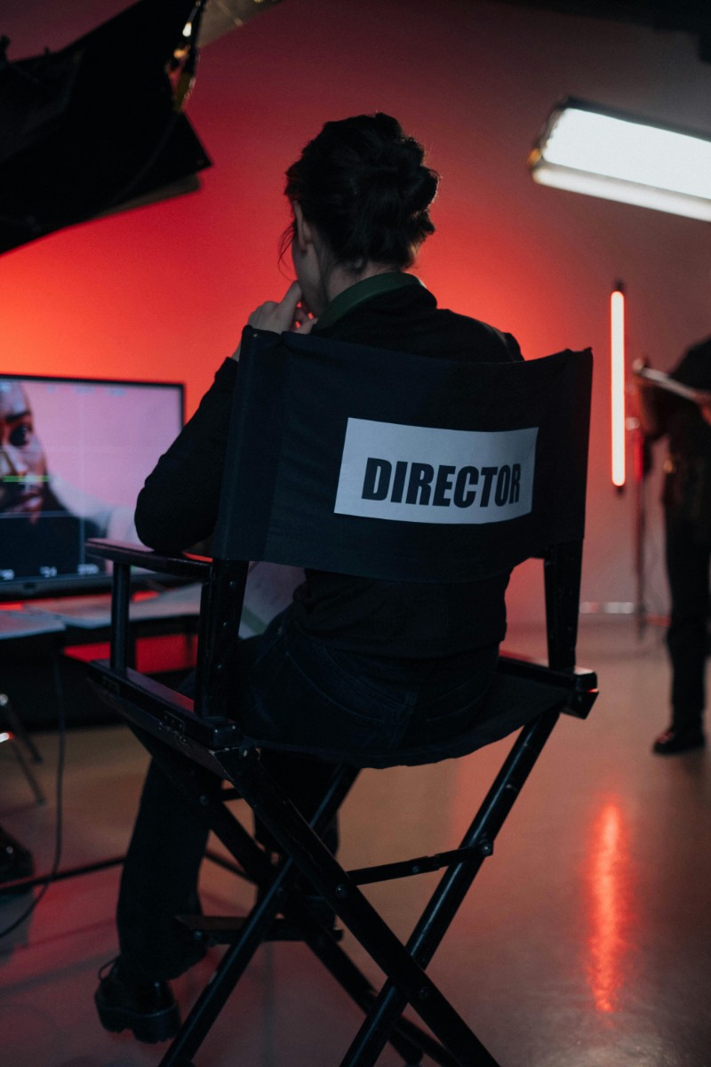 Person sitting on a director's chair facing a screen with a red-lit background in a film studio.