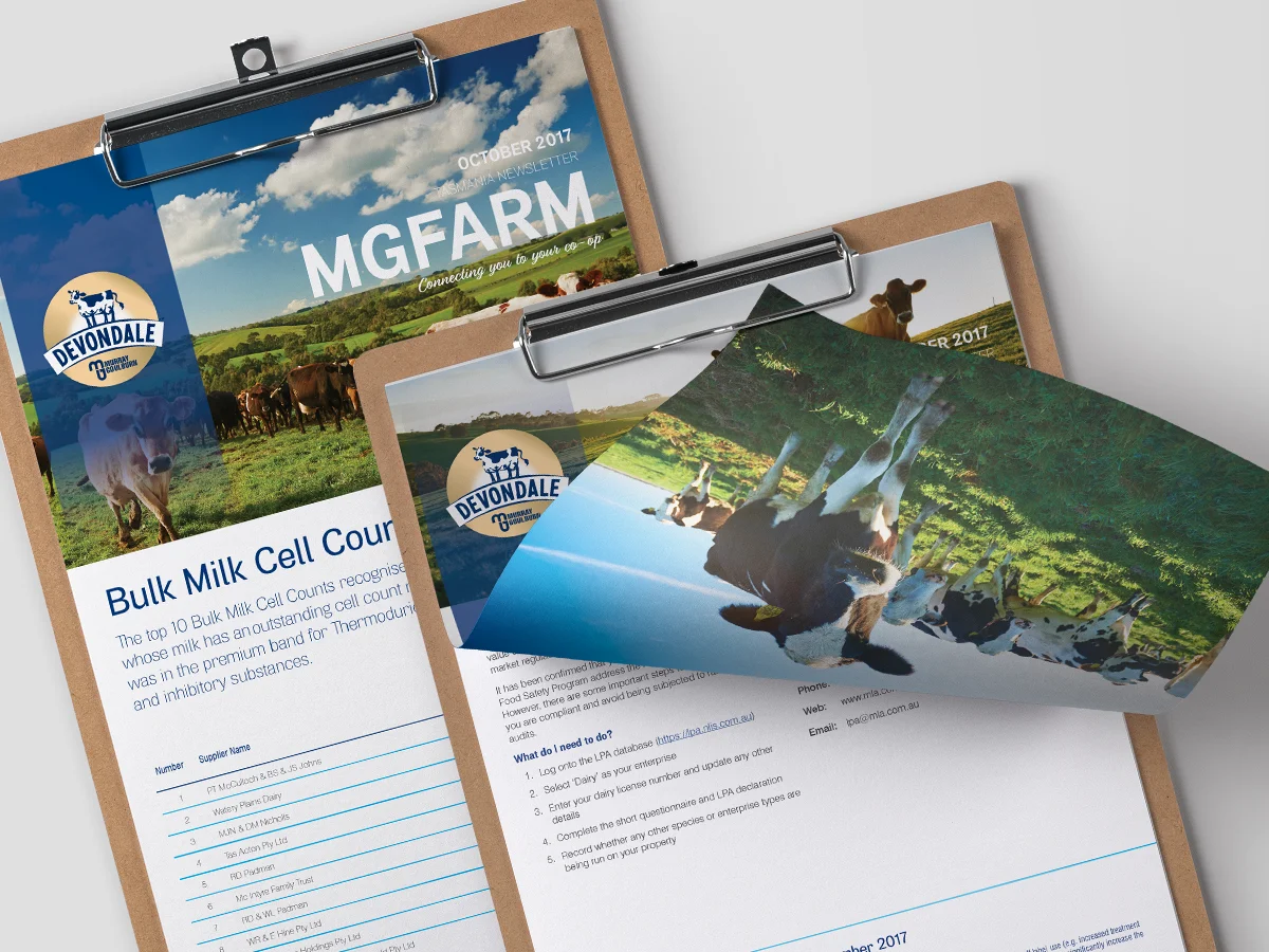 Two clipboards display Devondale MG Farm newsletters from October 2017 with images of cows grazing on green pastures.