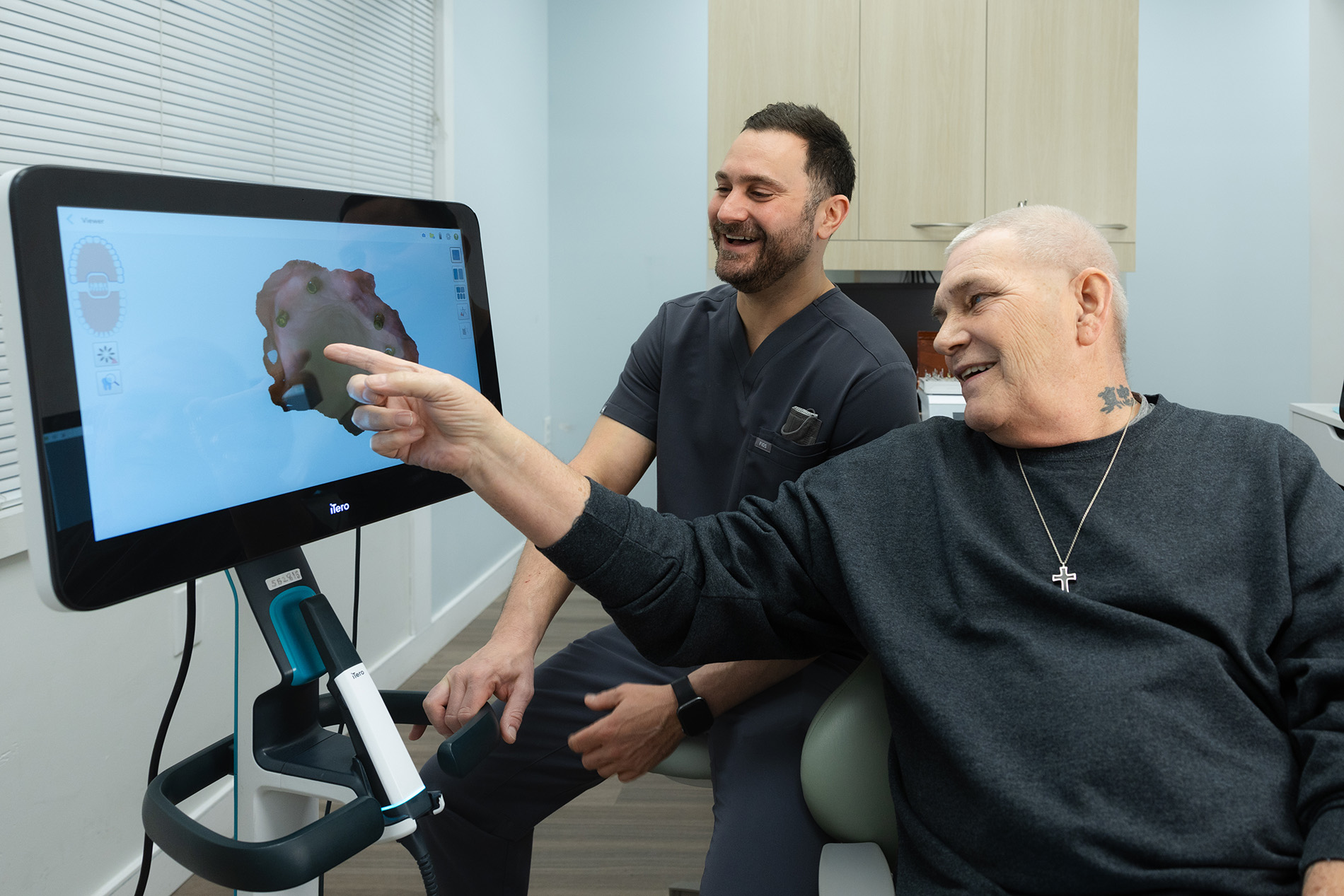 Dentist showing a smiling older male patient a dental scan on a digital screen in a clinic.