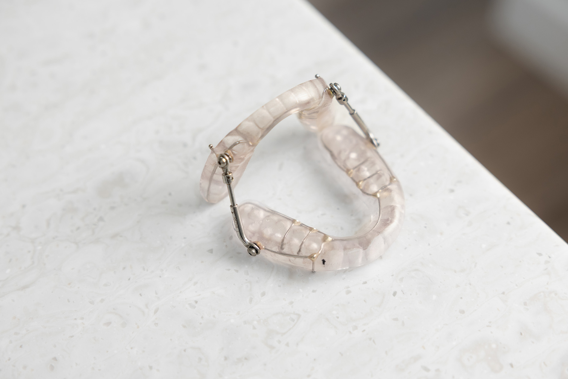 Transparent dental appliance with metal hinges resting on a white marble surface.