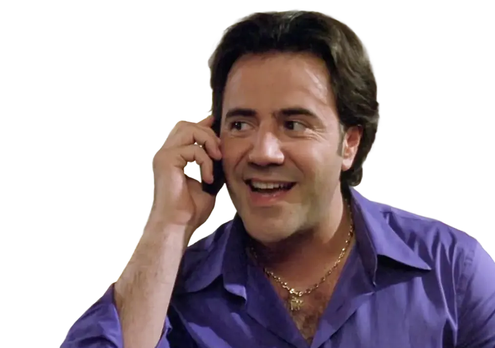 Man in a purple shirt smiling and talking on a phone.