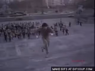 Personne courant en haut de larges marches extérieures en pierre avec un groupe de personnes derrière elle.