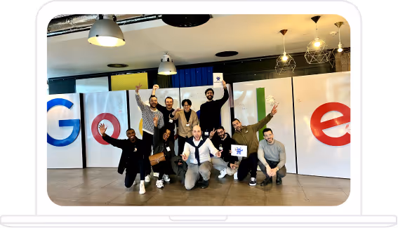 Groupe de personnes posant et souriant devant un grand logo Google à l'intérieur d'un espace de bureau moderne.