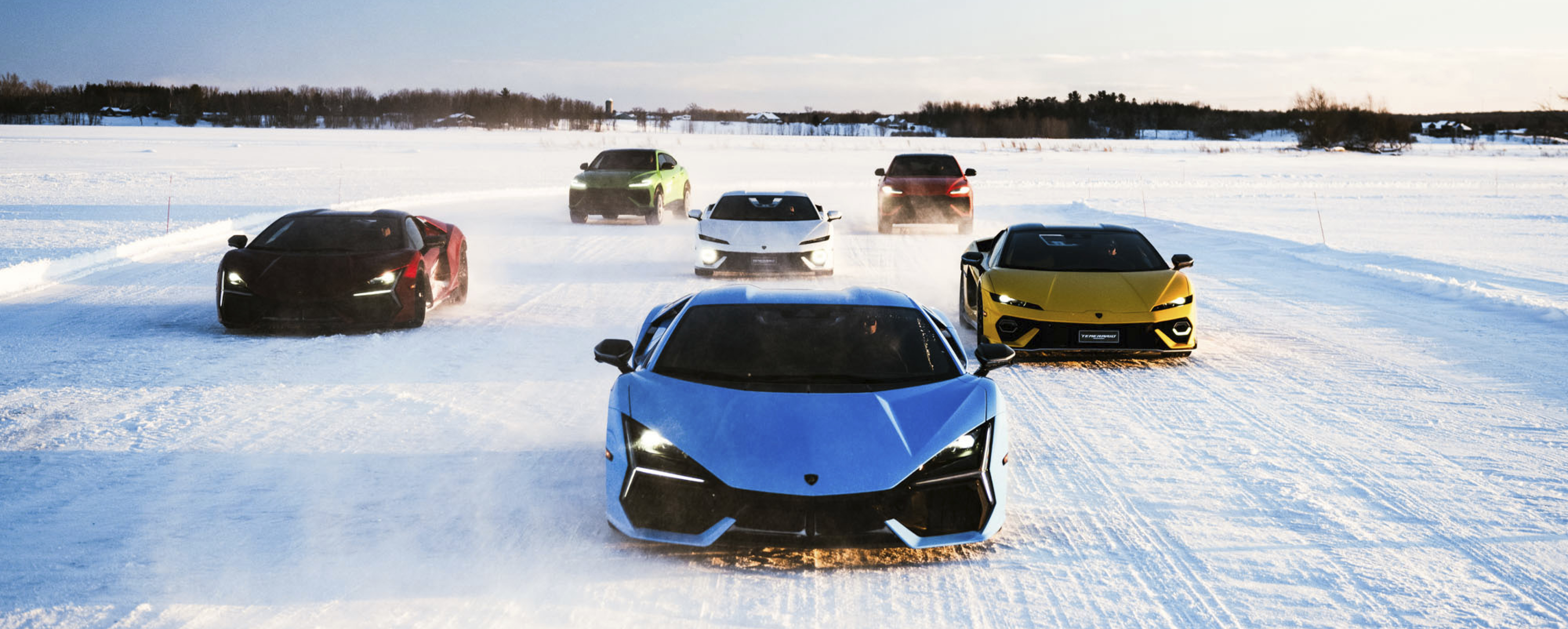 Fleet of Lamborghini vehicles driving toward camera on a snow-covered track, showcasing performance and control in winter conditions