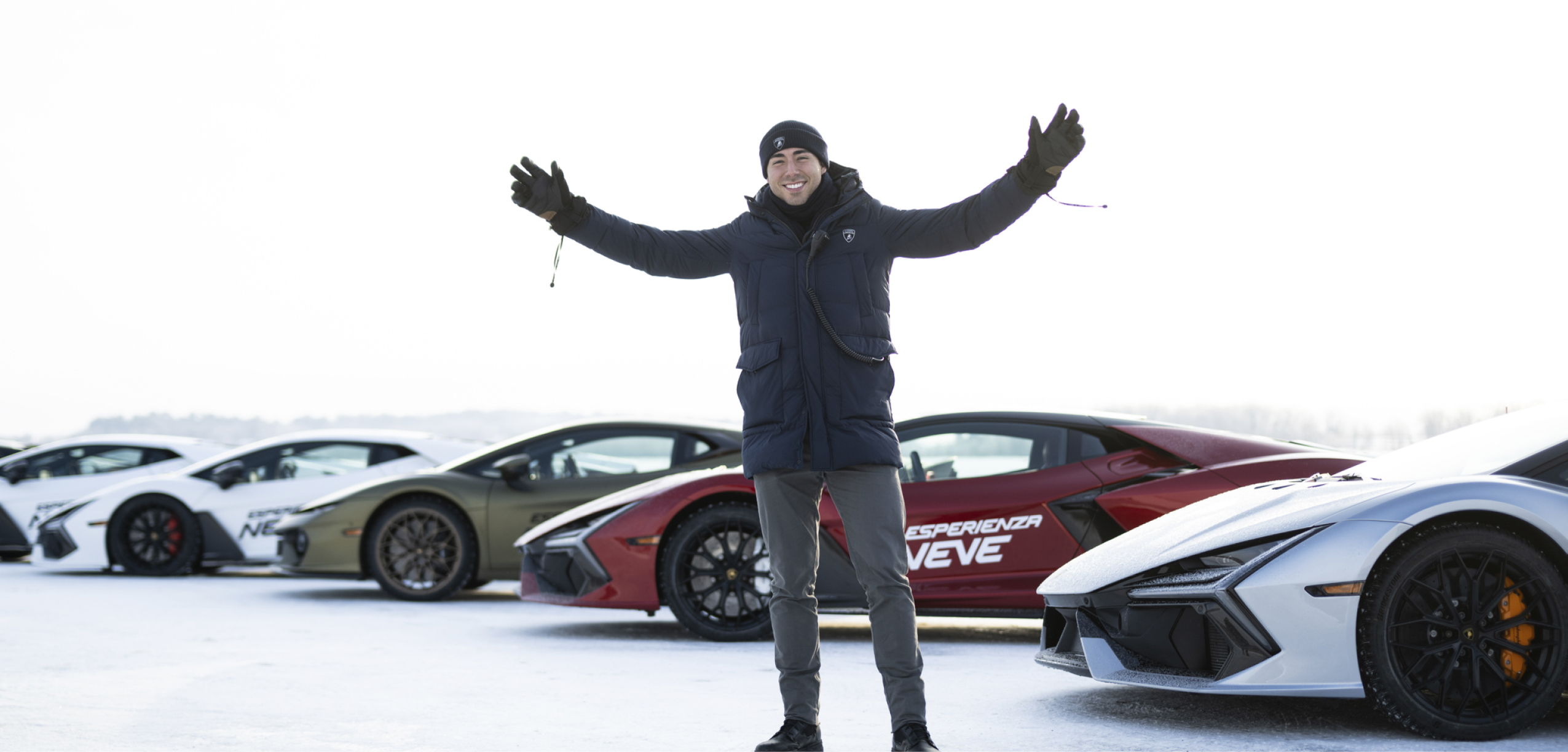 Lamborghini guest standing with arms wide in front of a lineup of supercars on ice, capturing the energy of the experience