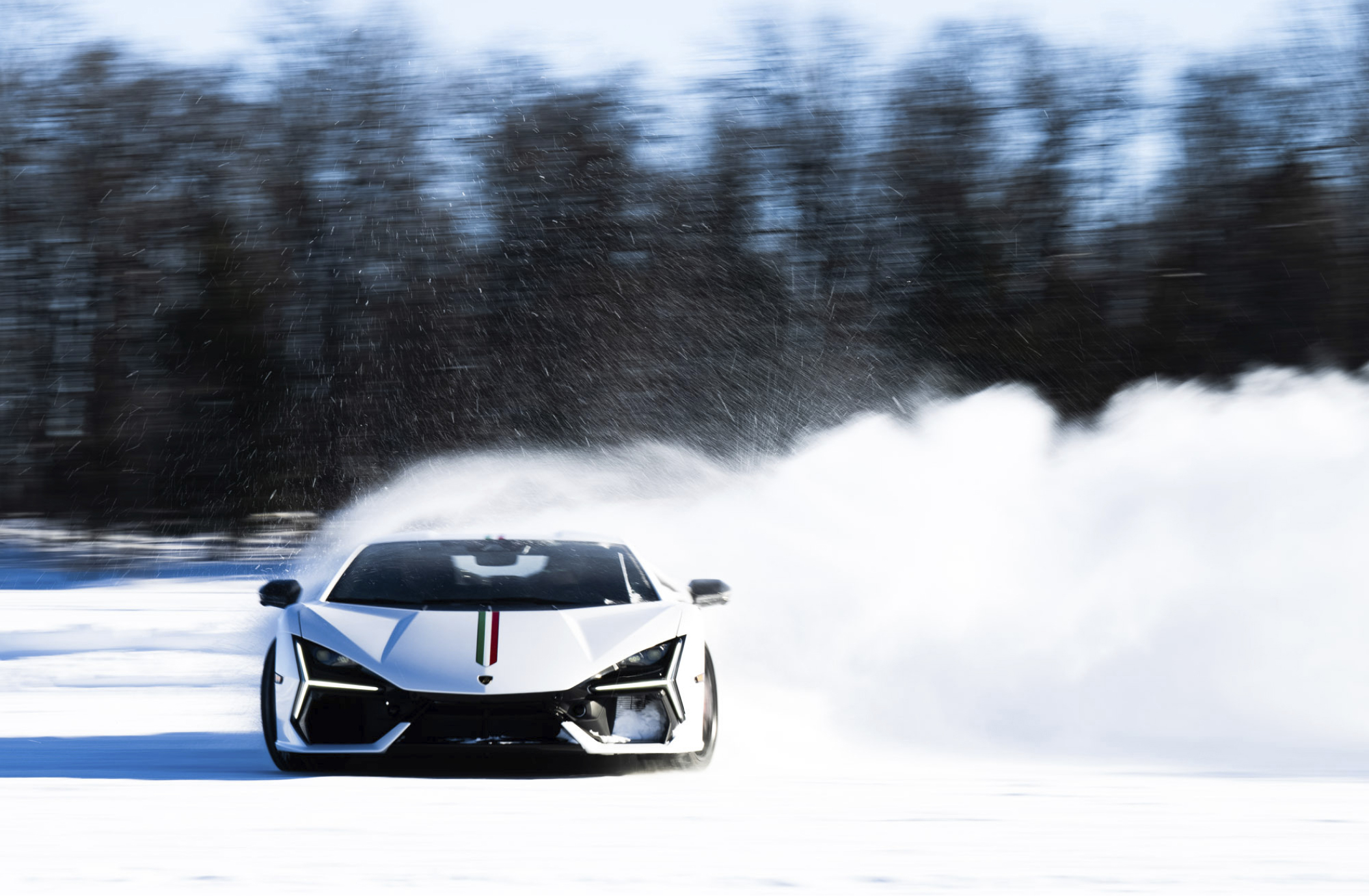 Lamborghini supercar drifting across a frozen track, kicking up a dramatic spray of snow against a forest backdrop