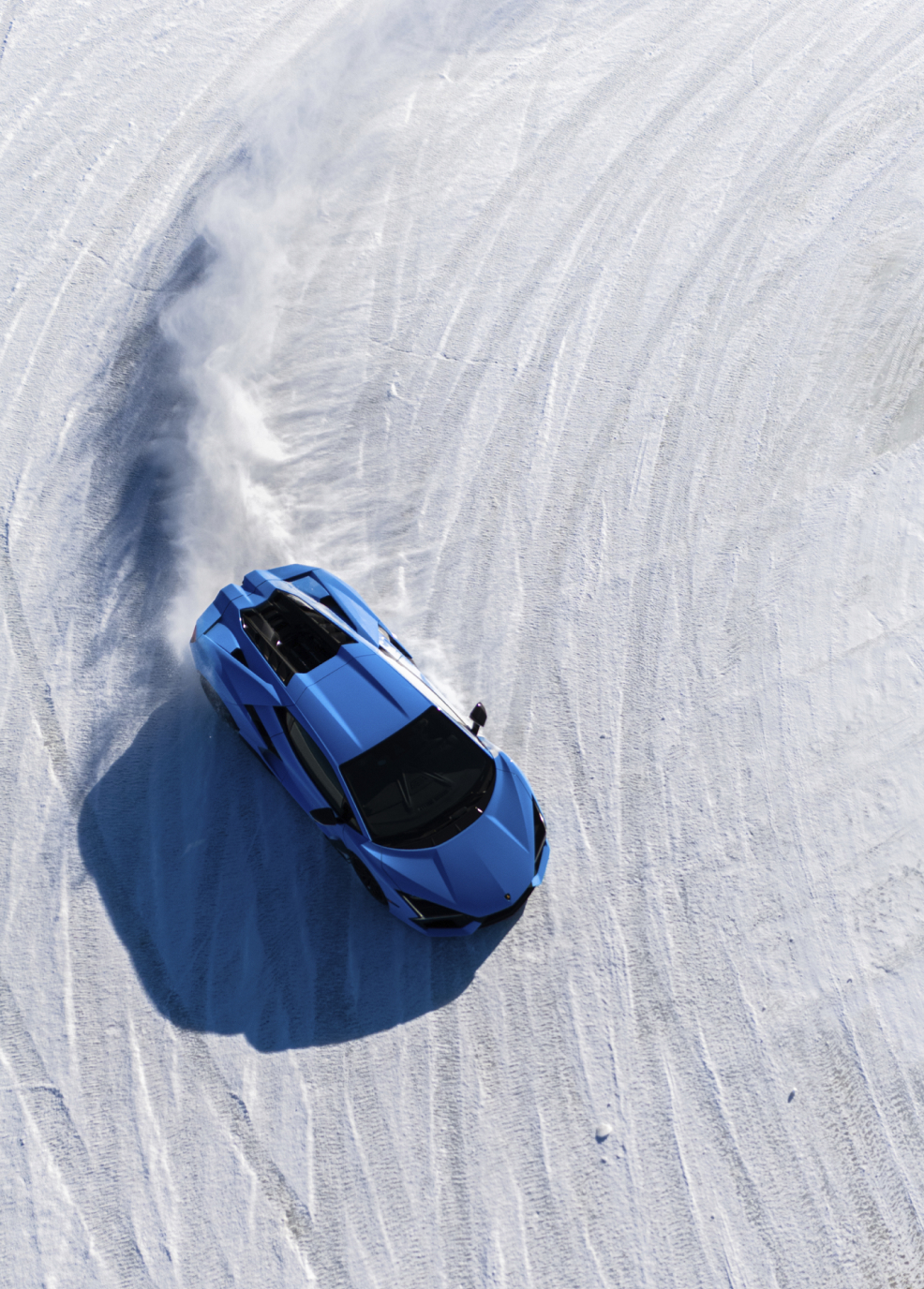 Aerial view of a blue Lamborghini carving precise tracks into an icy surface during a winter driving experience