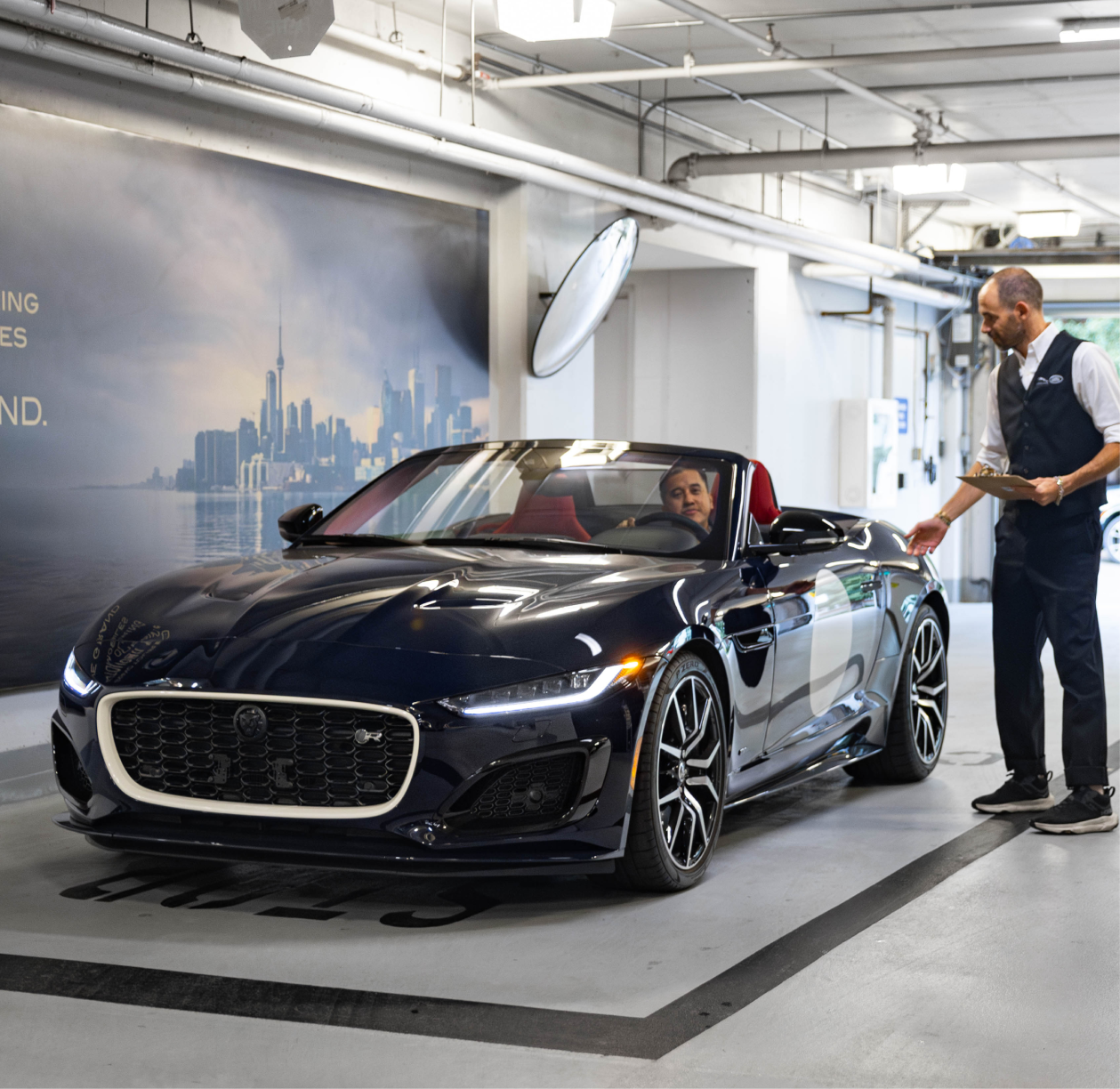Luxury Jaguar F‑TYPE convertible in dealership garage as concierge greets driver, illustrating JLR Toronto’s white‑glove service experience.