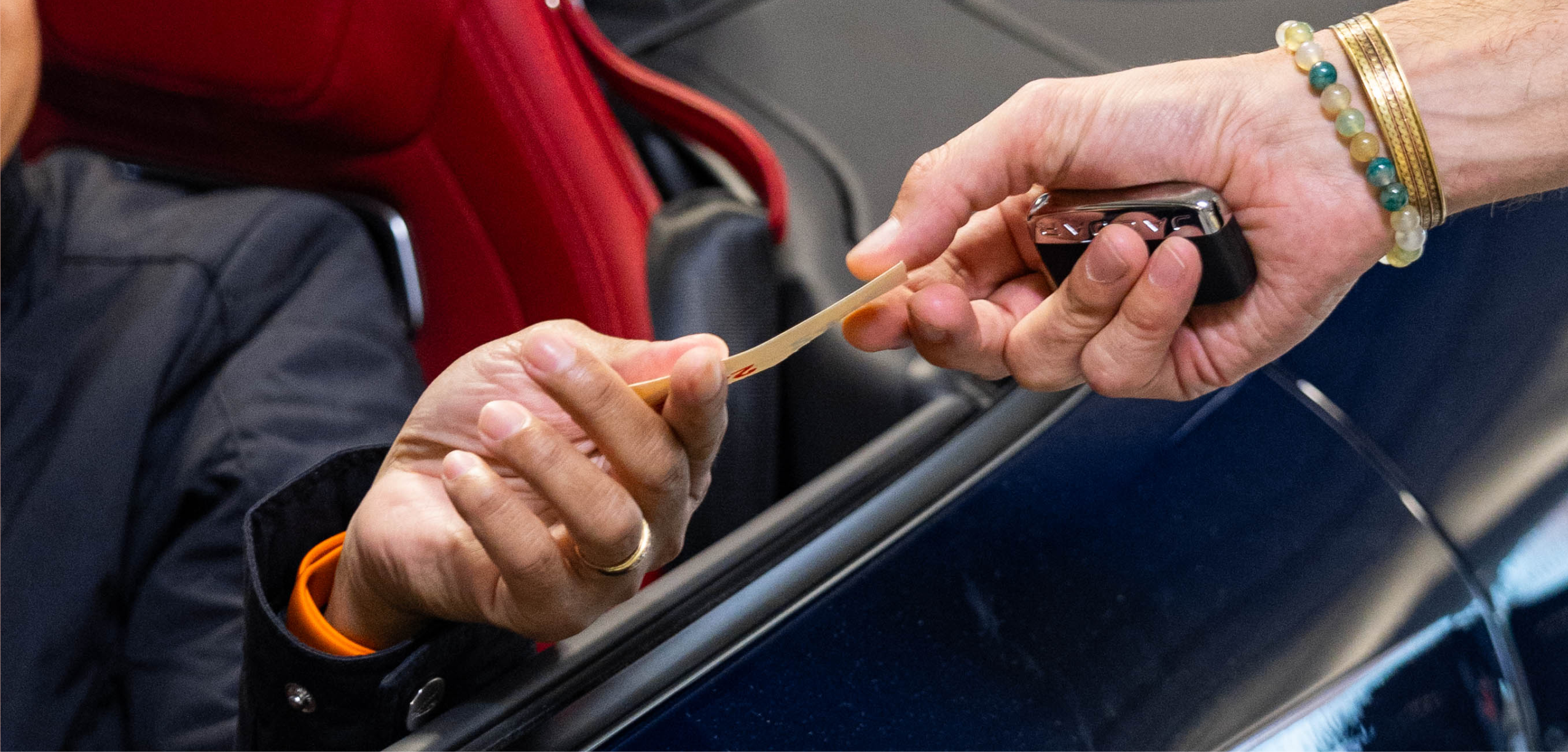 Close‑up of valet handing car key and ticket to driver inside red‑leather Jaguar, symbolizing premium customer handoff and personalized service.