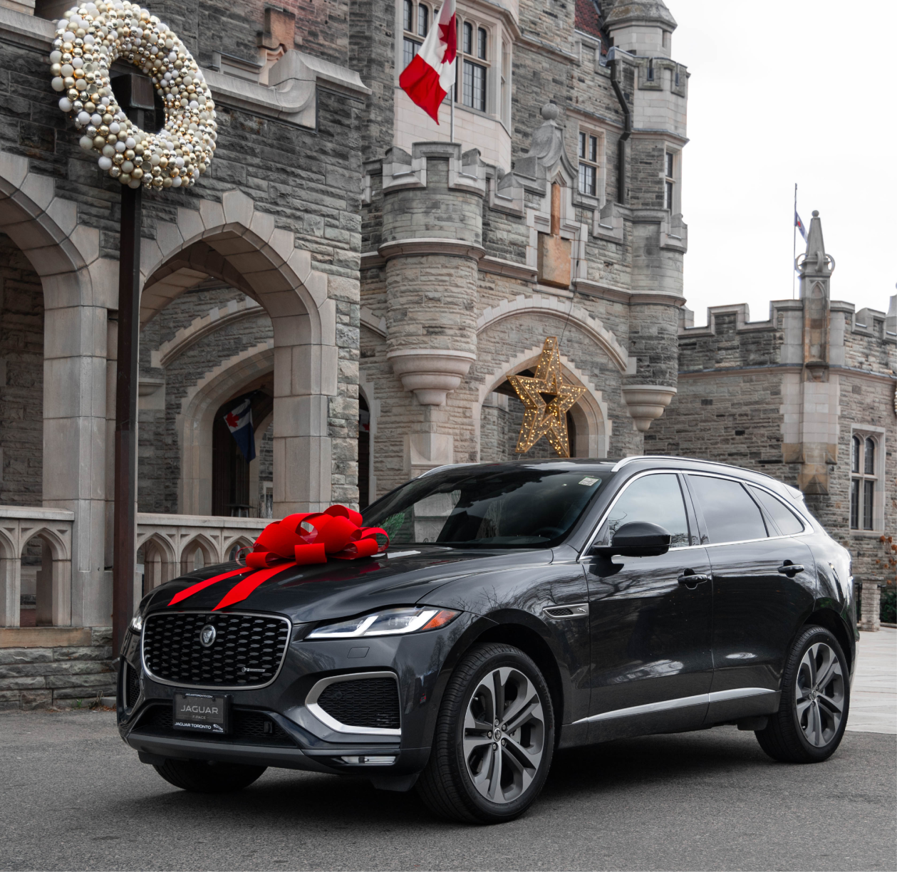 Jaguar SUV with red bow parked before castle‑style building decorated for holidays, reflecting festive luxury and dealership gifting campaign.