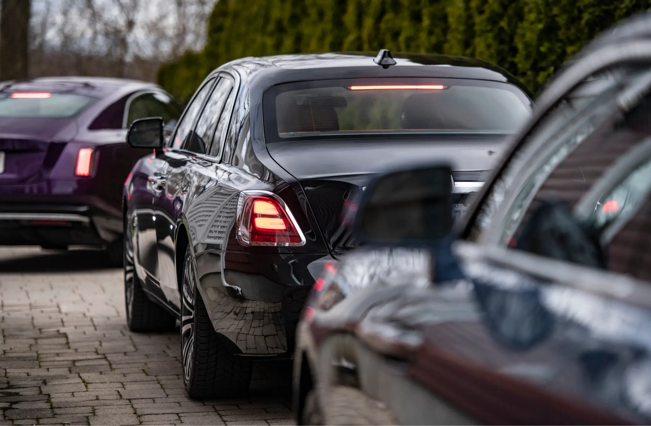 Three Rolls‑Royce sedans departing along a paved driveway with brake lights glowing, reflecting precision craftsmanship and coordinated luxury movement.
