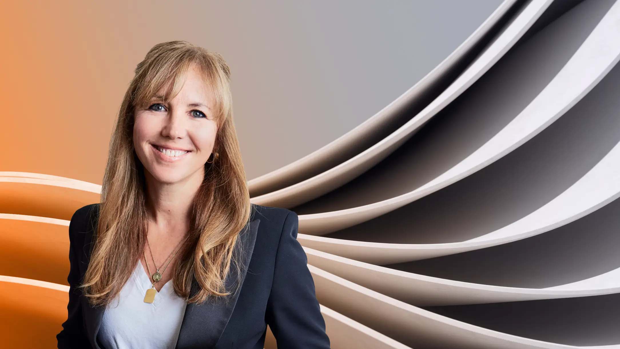 Natalie Maurice smiling in a navy blazer and white top before an abstract backdrop blending warm orange and cool gray tones, symbolizing creativity and balance.
