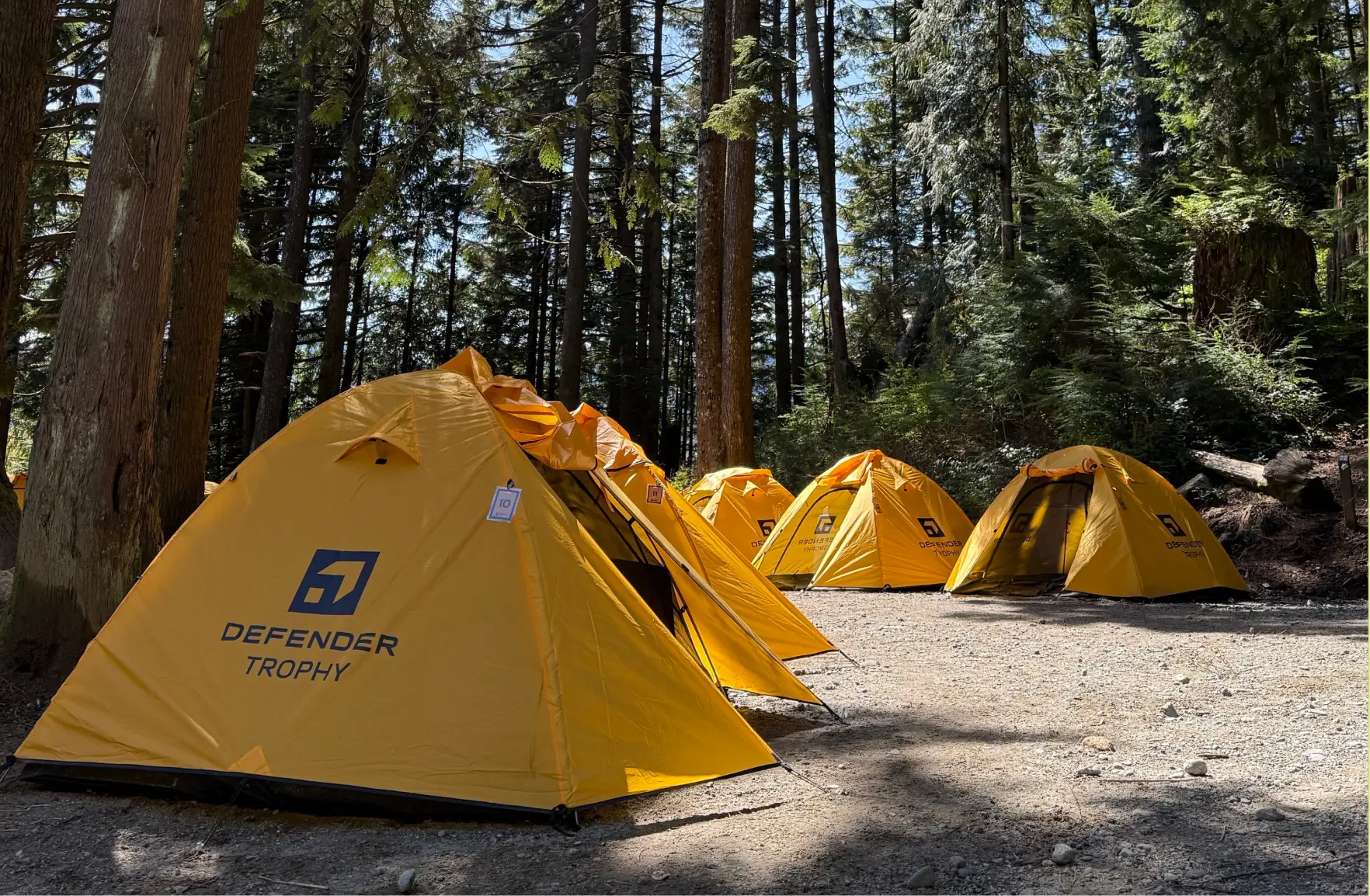Defender Trophy basecamp features organized participant tents in a forest setting, supporting a multi-day adventure competition.