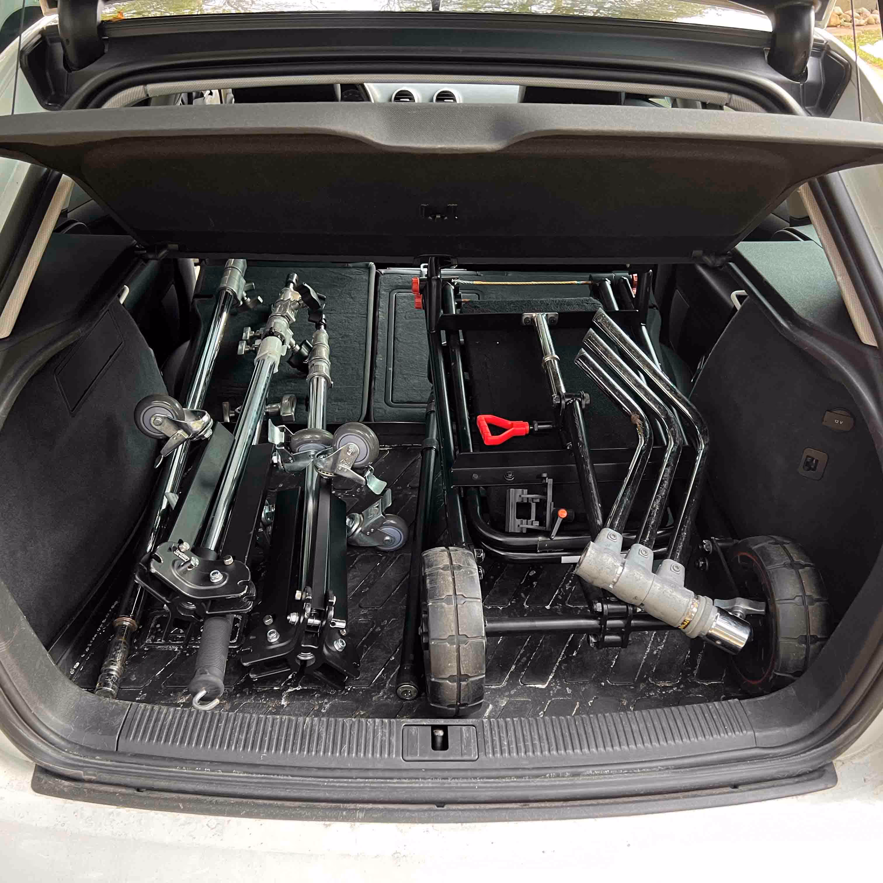 Car trunk open, showing folded black metal photography or film equipment stands and carts with wheels inside.