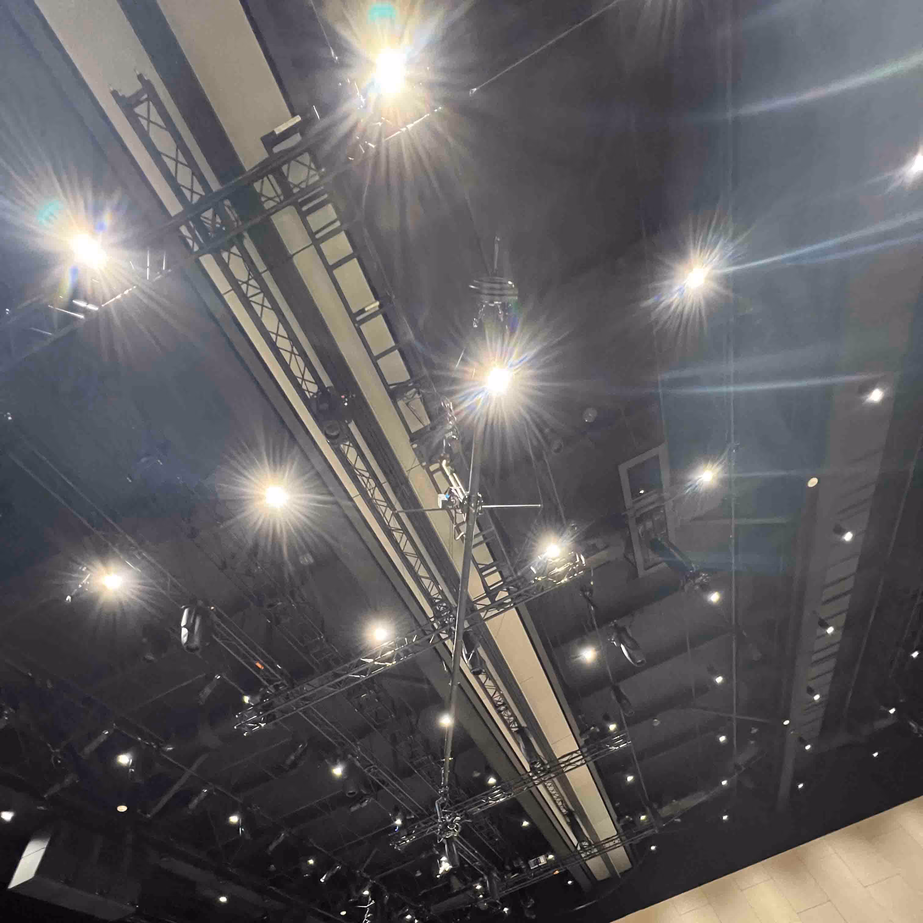 Ceiling with multiple stage lights and metal rigging beams in a dark indoor venue.