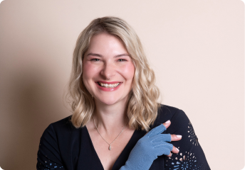 Smiling woman with blonde wavy hair wearing a black top and a blue fingerless glove on one hand.