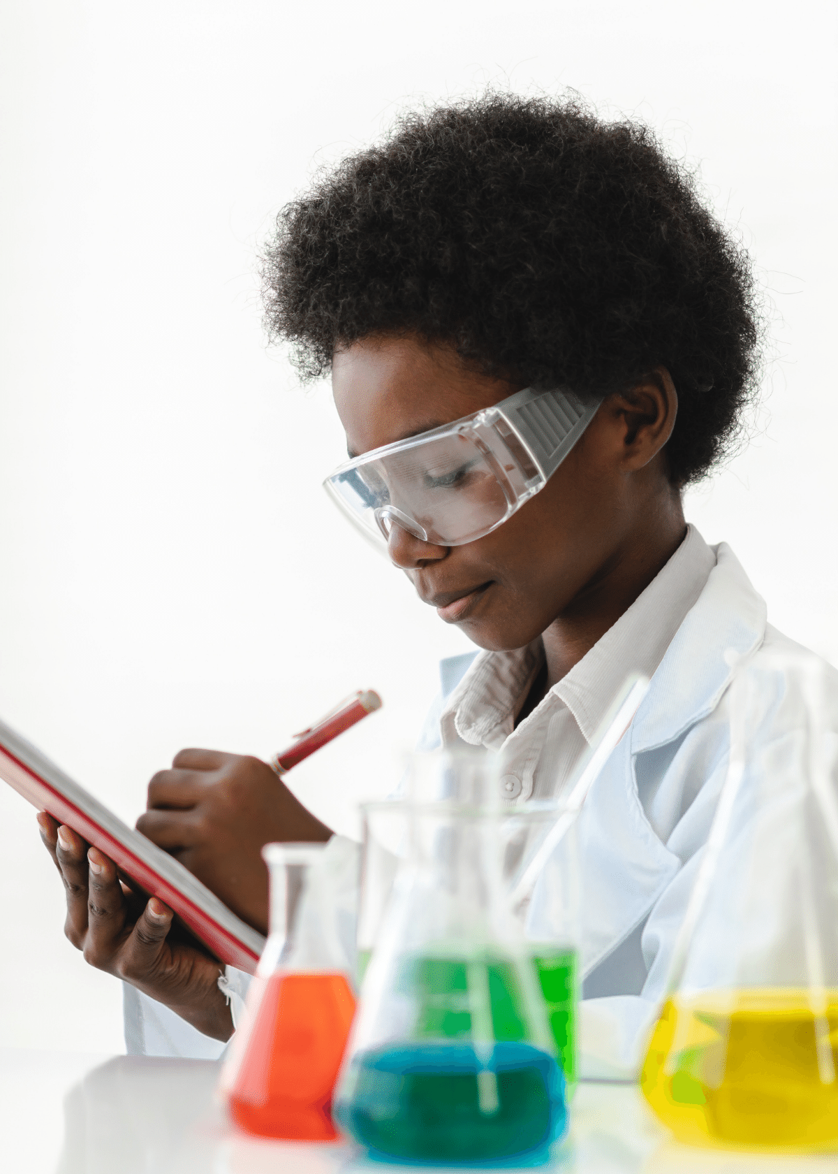 Young scientist wearing safety goggles and a lab coat, writing notes on a clipboard with colorful chemical liquids in beakers in the foreground.