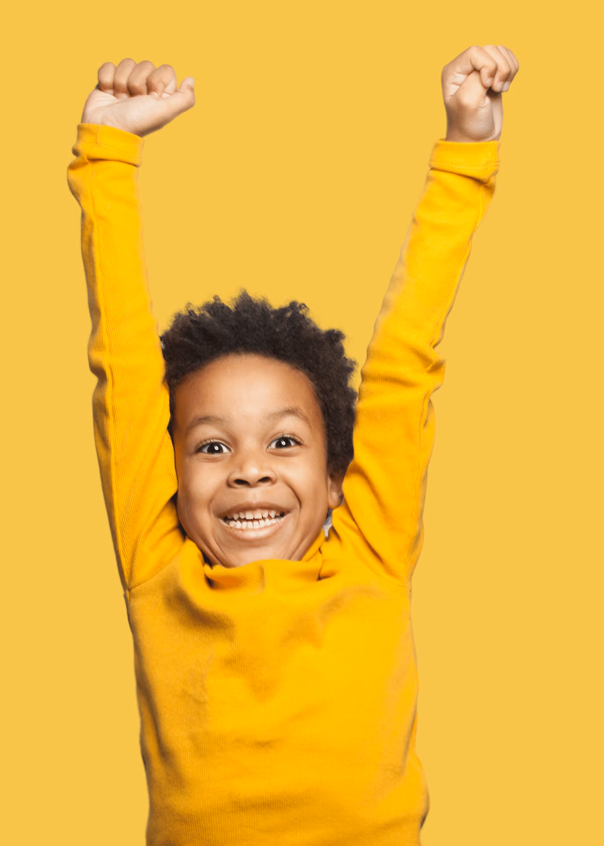 Excited young child with curly hair wearing a bright yellow long-sleeve shirt smiling and raising both arms against a yellow background.