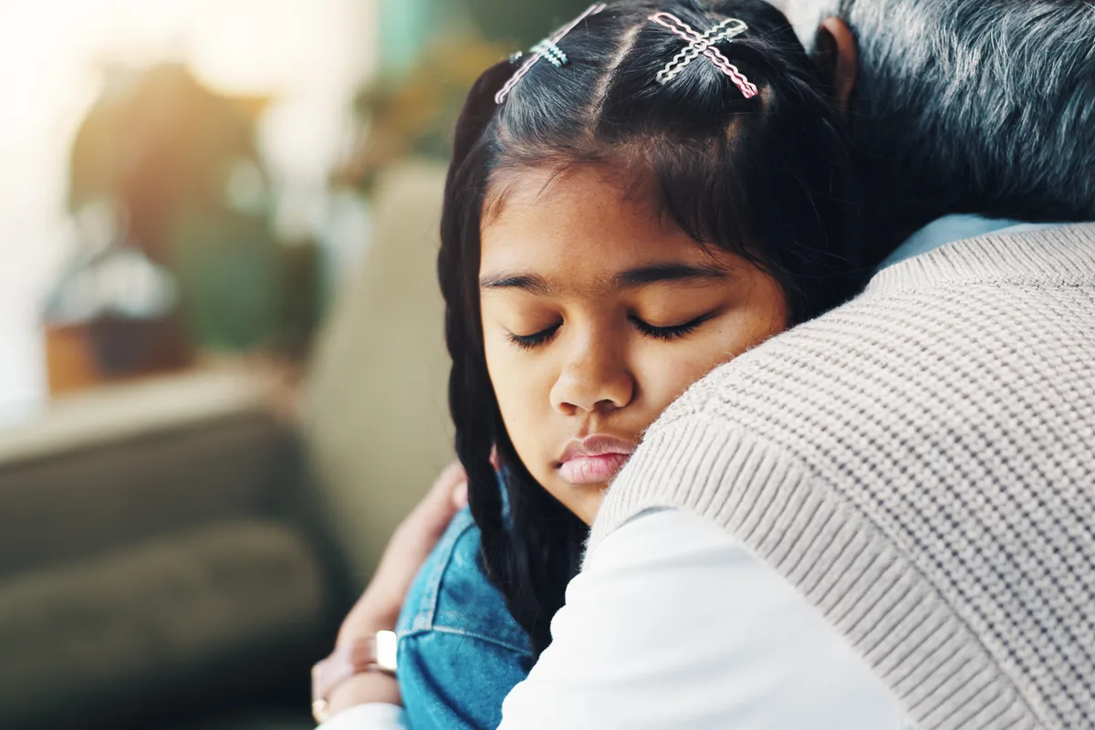 Child resting her head on a caregiver’s shoulder during a hug