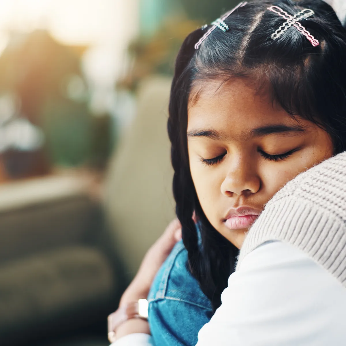 Child resting her head on a caregiver’s shoulder during a hug