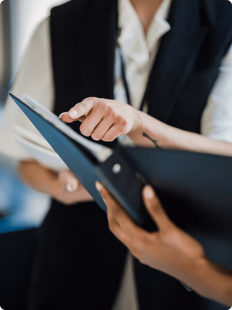 Two people reviewing documents in a black folder, one person pointing at the papers.