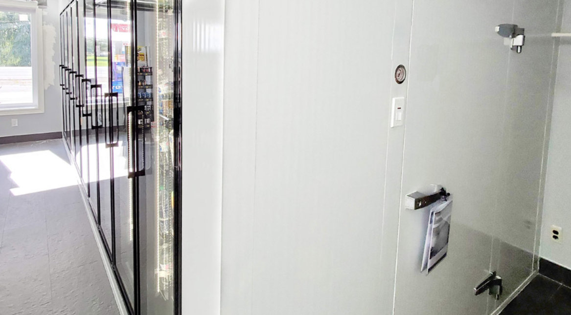 Couloir lumineux avec une rangée de vitrines réfrigérées à porte en verre à gauche et un mur blanc à droite.