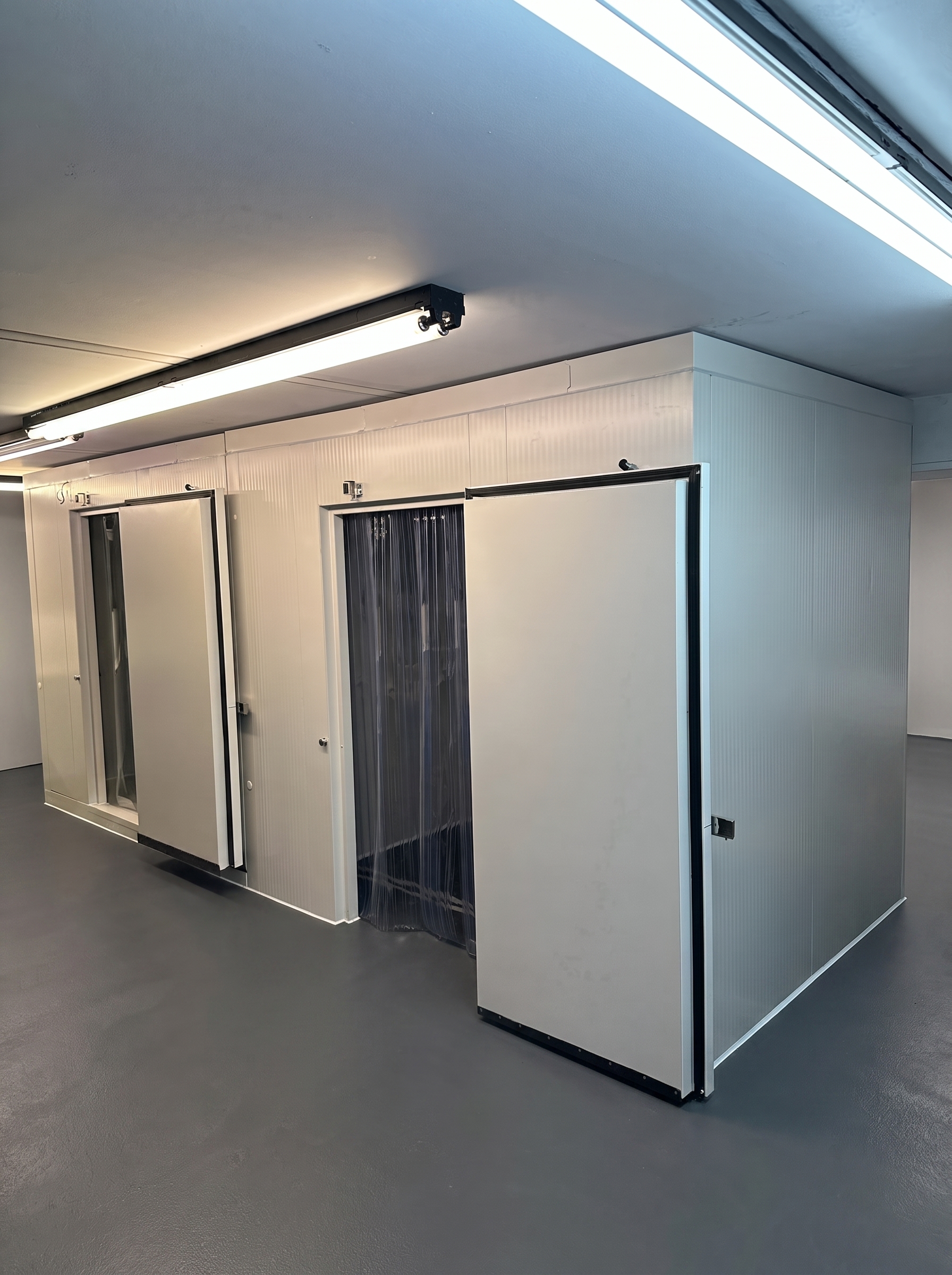 Couloir lumineux avec une rangée de vitrines réfrigérées à porte en verre à gauche et un mur blanc à droite.