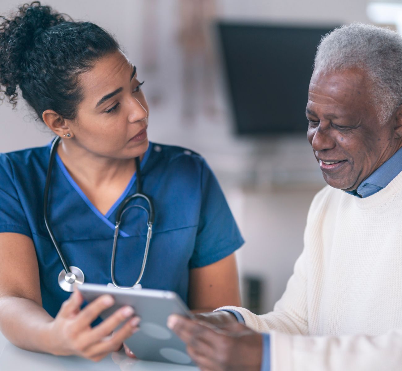a nurse with a stethoscope around her neck helps a patient read their chart 