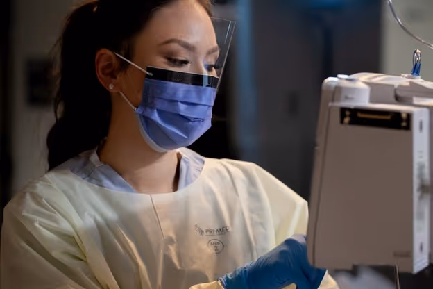 nurse wearing a visor face mask, gown, and gloves in the care environment