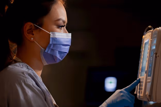nurse wearing face mask and gloves while adjusting IV pump