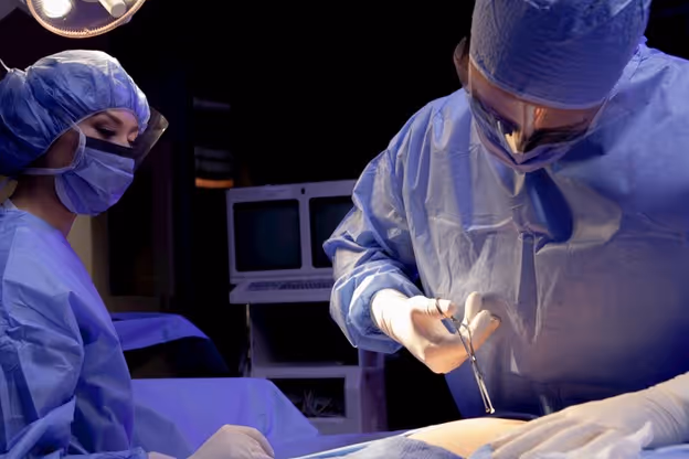 Surgeon and nurse wearing visor face mask, head covering, and gloves in operating room