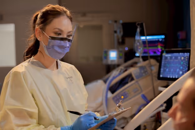 medical professional wearing visor face mask, gown, and gloves while recording chart information